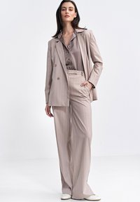 Jasnobeżowy garnitur w prążki z podwójnym zapięciem i szerokimi spodniami, w połączeniu z pasującą satynową bluzką. Gładka tekstura, dopasowany krój.