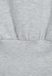 Tessuto di felpa grigio chiaro con una consistenza morbida e un leggero arricciamento in vita. Il materiale è elasticizzato e liscio.