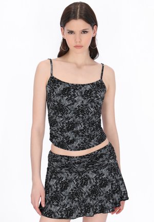 Tânără purtând un top fără mâneci și o fustă asortate, cu model de dantelă neagră, stând în picioare pe un fundal alb.