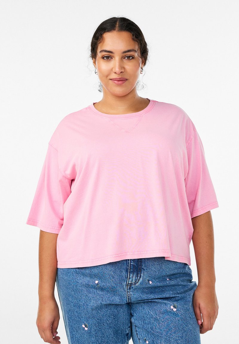 Lyserød, oversized T-shirt med korte ærmer, rund halsudskæring og en glat tekstur, parret med lyseblå jeans med dekorative detaljer.