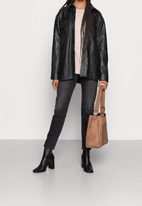 Czarna skórzana koszulowa kurtka, jasnobeżowy top, ciemne dżinsy i czarne botki na obcasie. Brązowa torebka z fakturowanym wykończeniem i regulowanym paskiem.