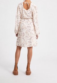 Vestido de estampado floral en crema claro, con mangas largas, un escote en forma de ojal en la parte posterior y una falda acampanada; combinado con botas de plataforma gruesas en marrón.