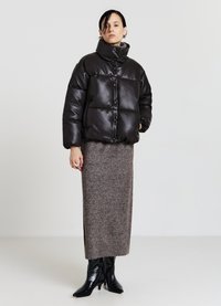 Giacca nera e morbida con colletto alto e dettagli dei bottoni, abbinata a una lunga gonna marrone texturizzata e stivali neri lucidi al ginocchio.