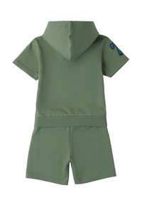 Combinaison à manches courtes, à capuche, de couleur vert olive. Fabriquée en tissu doux avec une taille ajustée et des shorts. Présente un écusson avec un numéro bleu sur le bras gauche.