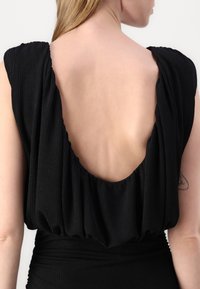 Black dress featuring a deep back cutout, ribbed texture, and draped fabric around the shoulders, creating a soft silhouette.