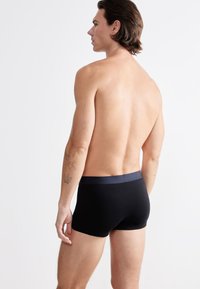 Mustat boxerit, joissa on tummansininen vyötärö, pehmeästä materiaalista valmistetut, tarjoavat tiukan istuvuuden ja minimalistisen suunnittelun ilman kuvioita.