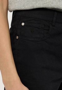 Svarta denimjeans har en klassisk femfickedesign, silverdetaljer och subtila sömnadsdetaljer som framhäver en ren, modern silhuett.