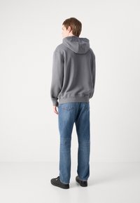 Grijze hoodie met een relaxte pasvorm, gecombineerd met een blauwe spijkerbroek en zwarte sneakers. Soepele stof en eenvoudig ontwerp.