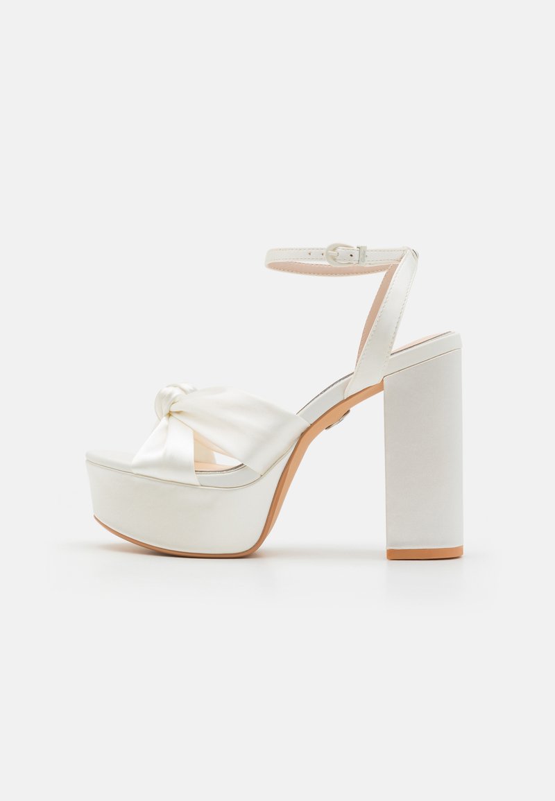 White satin platform heel with a knotted design on the front, ankle strap, and a chunky block heel. Smooth texture with a polished finish.