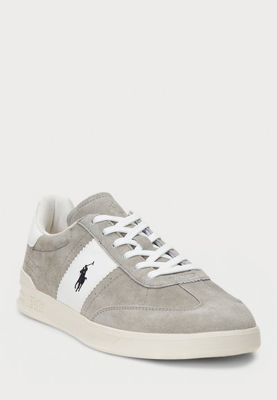 Szürke velúr sneaker fehér kiegészítőkkel, fűzős dizájnal, gumitalppal és kis logó részlettel az oldalon.