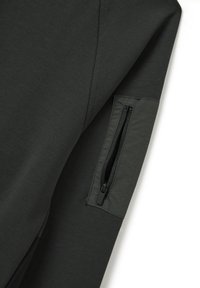 Gara a maniche lunghe di colore grigio scuro con una tasca con cerniera sul braccio sinistro. Realizzata in un tessuto leggero e liscio con una sottile trama.