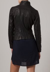 Czarna skórzana kurtka z wysokim kołnierzem, dopasowanym krojem i widocznymi detalami szwów, noszona na ciemnoniebieskiej sukience.