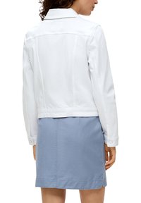 Witte spijkerjack met een aansluitende pasvorm, knopenmanschetten en een cropped lengte, gecombineerd met een lichtblauwe rok. Zichtbare stiksels en zakken.