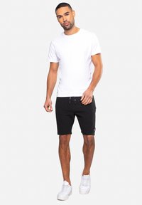 Witte crew-neck t-shirt gecombineerd met zwarte shorts van een gestructureerde stof met trekkoord. Afgemaakt met witte sneakers.