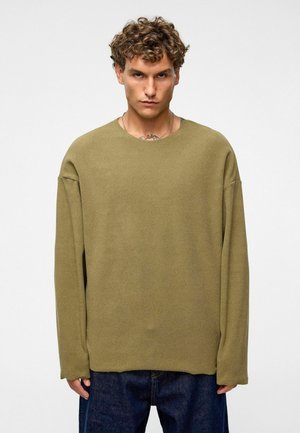 Olijfgroen oversized sweater met een ronde hals, verlaagde schouders en een zachte textuur. Gecombineerd met donkere jeans voor contrast.