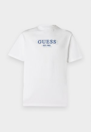 Camiseta blanca de manga corta con el texto azul en capas "GUESS EST. 1981" centrado en el pecho.