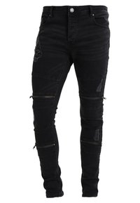 Jeans negros de corte ajustado con parches desgastados y múltiples cremalleras horizontales en ambas piernas.
