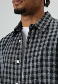 Zwart- en grijs geruit flanellen overhemd met knopen aan de voorkant, witte knopen en een klassiek kraagje, met een zachte textuur en een casual ontwerp.