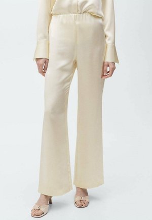 Satin, cream-colored trousers with an elastic waistband and wide legs. Smooth texture and minimal seams. Paired with light-colored heels.