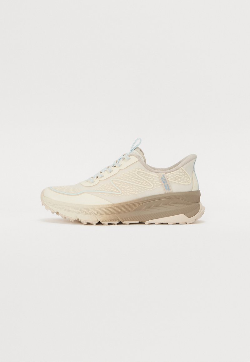 Zapatilla de running en crema con parte superior texturizada, acentos en azul claro y una suela gruesa de color marrón claro. Incluye cordones y una lengüeta en el talón.