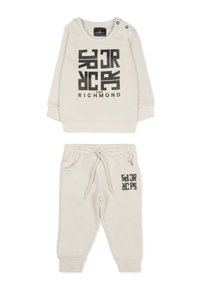 Jasny beżowy dres dla małego dziecka z czarnym nadrukiem graficznym. Zawiera bluzę z długim rękawem z zapięciem na ramionach oraz spodnie z elastycznym pasem i kieszeniami.