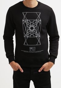 Sweat-shirt noir en matériau doux, avec un design graphique blanc géométrique à l'avant et des poignets et un col côtelés.