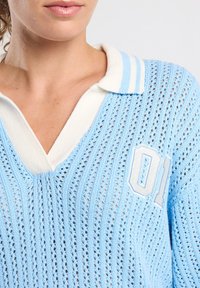 Light blue knitted sweater with a V-neck and a white striped collar, featuring an embroidered "01" on the left chest in white.