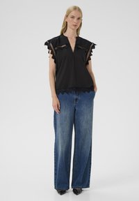 Sort bomuldsbluse med flæser ved ærmerne og gennemsigtige detaljer; parret med vide blå jeans. Glat tekstur med et flydende design.