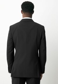 Chaqueta de traje negra con una abertura sencilla, ajuste entallado y textura suave. Presenta solapas muesca y detalles sutiles en los puños.