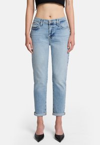 Jeans in denim blu chiaro con gamba dritta, orli risvolti, cinque tasche e leggero sbiadimento. Indossati con un top corto nero e scarpe scure a punta.