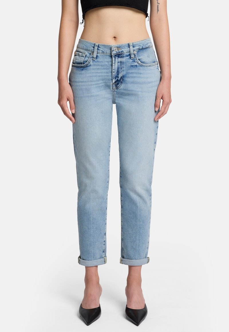Jeans in denim blu chiaro con gamba dritta, orli risvolti, cinque tasche e leggero sbiadimento. Indossati con un top corto nero e scarpe scure a punta.