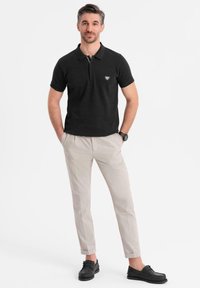 Černé polo tričko s krátkým rukávem a zipovým límcem, spárované se světle béžovými úzkými kalhotami a černými botami.