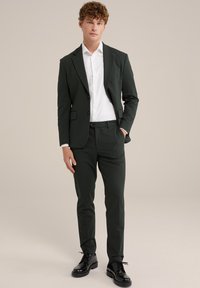 Costum verde închis cu un design slim-fit, asortat cu o cămașă albă și pantofi negri. Materialul pare neted, cu un finisaj mat.