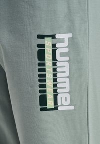 Lichtgroene sportkledingstof met "Hummel Sportswear" logo in witte en zwarte letters op de zijnaden.