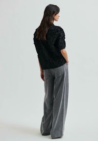 Blusa nera con texture e dettagli floreali, abbinata a una comoda jeans a gamba larga grigi, vista da una prospettiva posteriore.