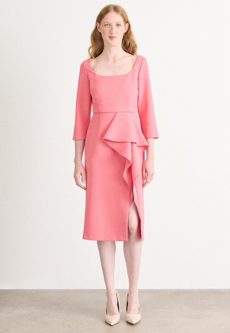 Robe rose mi-longue avec des manches trois-quarts, présentant un détail de volants à l'avant et une fente sur le côté, fabriquée dans un tissu lisse.