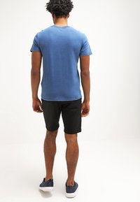 T-shirt en coton bleu avec un col rond, associé à un short noir. Vu de l'arrière, avec des manches courtes et une coupe décontractée.