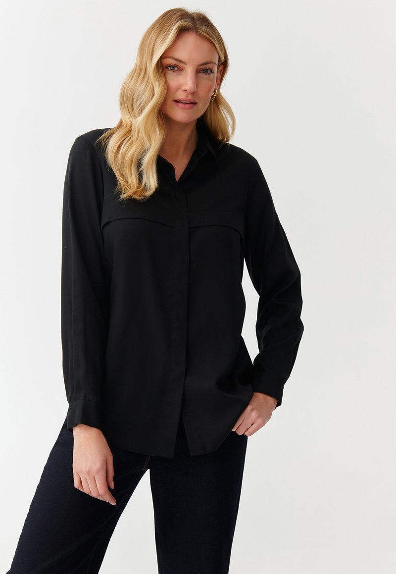 Long-sleeve black button-up shirt made of smooth fabric, featuring a classic collar and two chest pockets. Simple, minimal design.