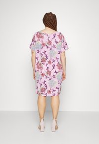 Růžové šaty s květinovým vzorem a krátkým rukávem, volného střihu, s detailem knoflíku na zadní straně, doplněné o světlé růžové sandály na vysokém podpatku.