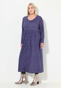 Abito viola a maniche lunghe con vita arricciata, caratterizzato da un motivo floreale. Indossato con stivaletti argentati lucidi e collant neri.