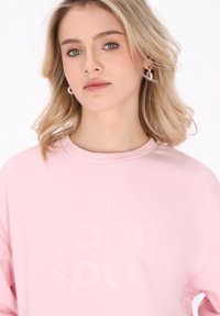 Felpa rosa chiaro con collo tondo, caratterizzata da una stampa in tessuto leggermente rialzata che recita "Possiedo un ANIMA MORBIDA." Tessuto morbido.