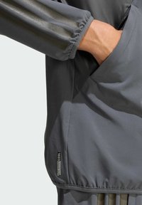 Šedá športová bunda s hladkým materiálom, elastickými manžetami, bočnou vreckom a reflexnými pruhmi na rukávoch. Prítomné logo ClimaCool.