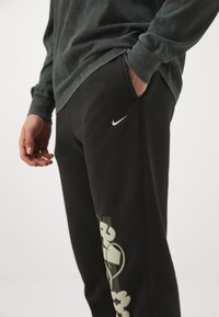 Los pantalones deportivos negros de Nike cuentan con un diseño impreso con acentos de color claro en la pierna izquierda. El material parece suave y elástico.