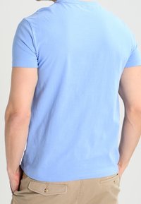 Světle modré bavlněné tričko s krátkými rukávy, kulatým výstřihem a jednoduchým designem. Tkanina vypadá měkká a mírně texturovaná.