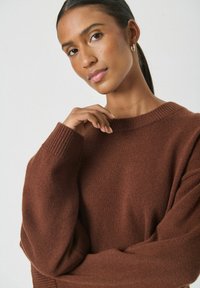 Brązowy sweter dzianinowy z prążkowanym okrągłym dekoltem i szerokimi rękawami, prezentujący miękki materiał i luźny krój.