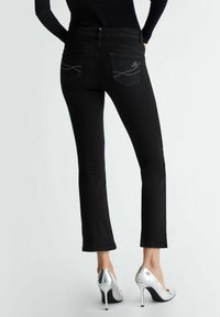 Jeans en denim noir avec une coupe slim, taille mi-haute, deux poches arrière avec une couture décorative et un accent subtil en logo argenté.