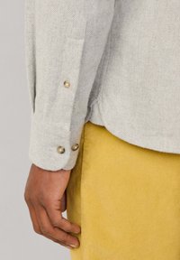 Camisa de espiga gris claro con puños abotonados, que presenta un tejido texturizado. Combinada con pantalones de pana amarillos, que exhiben un patrón de acanalado.