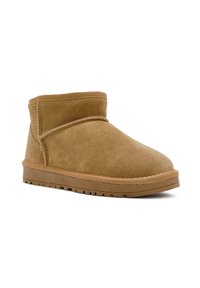 Beige Wildleder-Ankle-Boot mit einfachem Design, abgerundetem Zeh, flacher Gummisohle und gestickten Akzenten entlang der Naht.