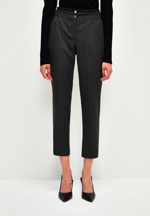 Femme portant un pantalon court gris foncé à fines rayures avec une fermeture à double bouton et des escarpins slingback noirs à bout pointu.