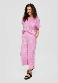 Ensemble deux pièces à motif floral rose comprenant un haut à manches courtes et un pantalon à jambes larges. Fabriqué en tissu léger avec des poches. Sandales noires.